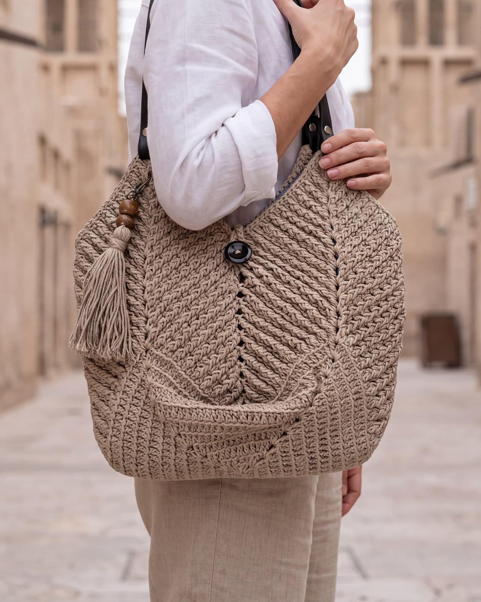 Mulher de camisa de linho branca com a bolsa Dubai cor areia no ombro, numa viela de arenito, imagem ilustrativa