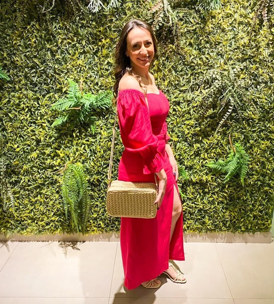 Cliente de vestido vermelho com a bolsa Sardenha dourada a tiracolo, diante de um jardim vertical