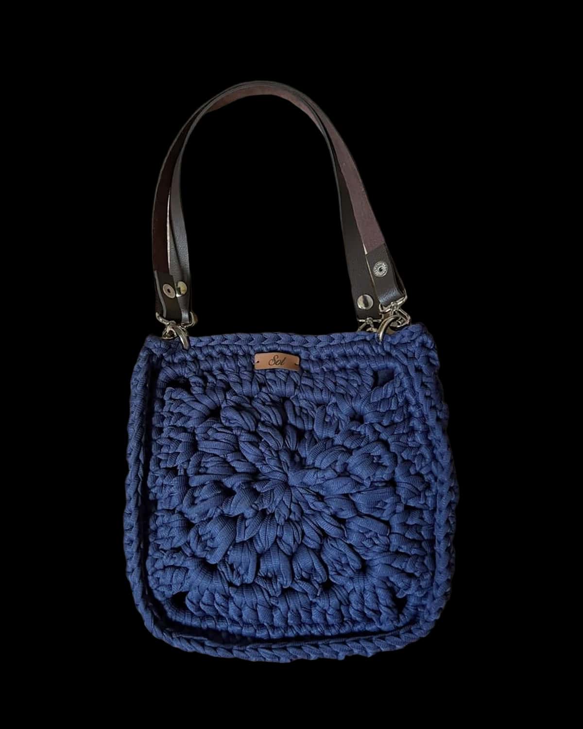 Bolsa Paris quadrada azul-marinho com flor de crochê em relevo e duas alças tipo couro, foto de catálogo em fundo neutro