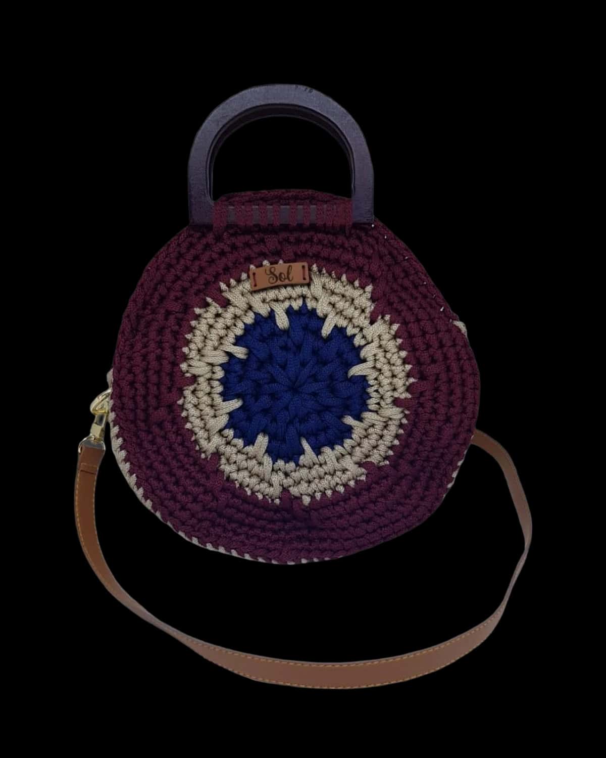 Bolsa Santorini redonda em crochê vinho com olho grego azul no centro, alça de mão em madeira e alça tipo couro, foto de catálogo em fundo neutro