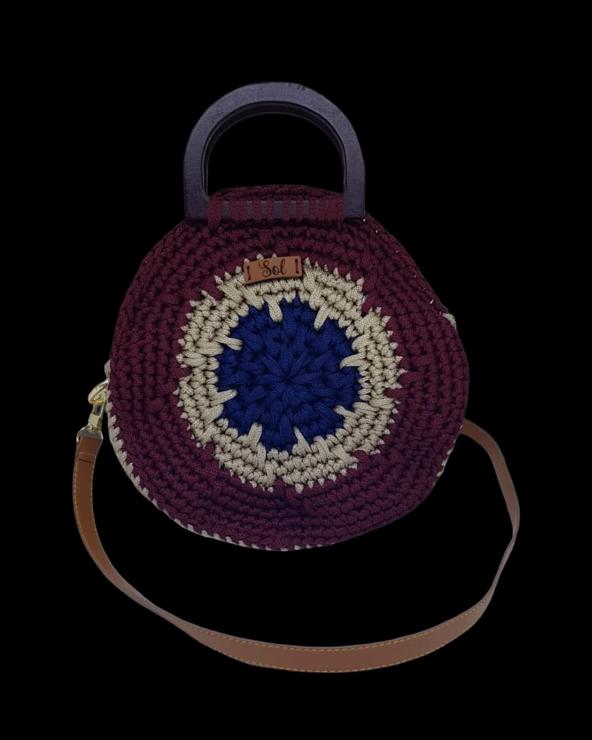Bolsa Santorini redonda em crochê vinho com olho grego azul no centro, alça de mão em madeira e alça tipo couro, foto de catálogo em fundo neutro