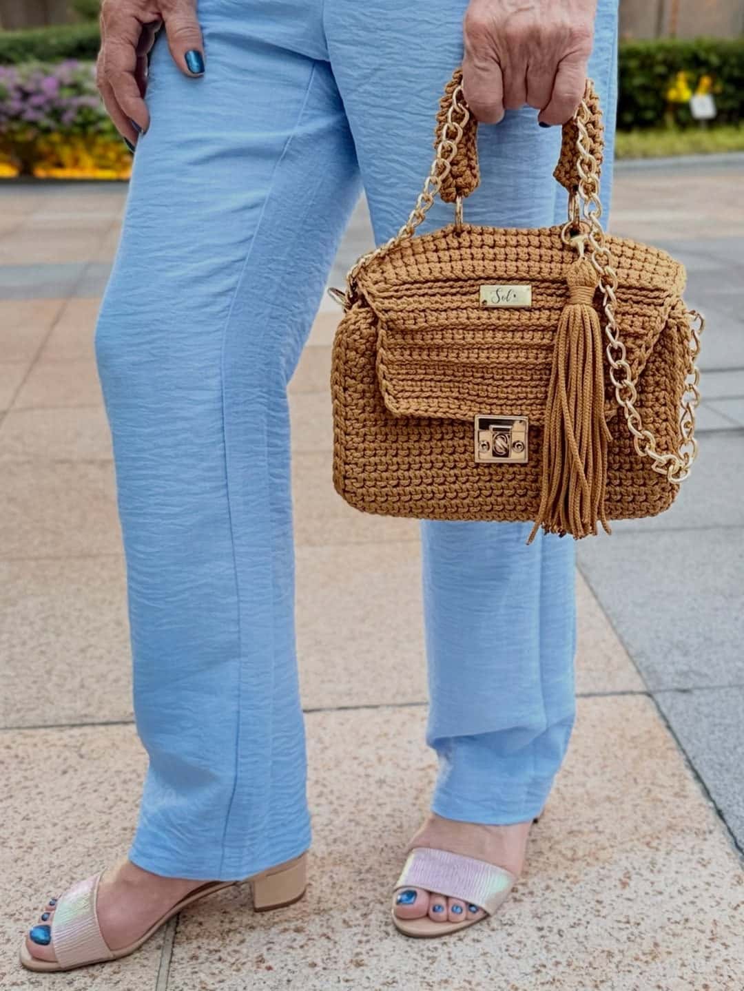 Detalhe da bolsa Siena caramelo na mão, com calça azul-clara